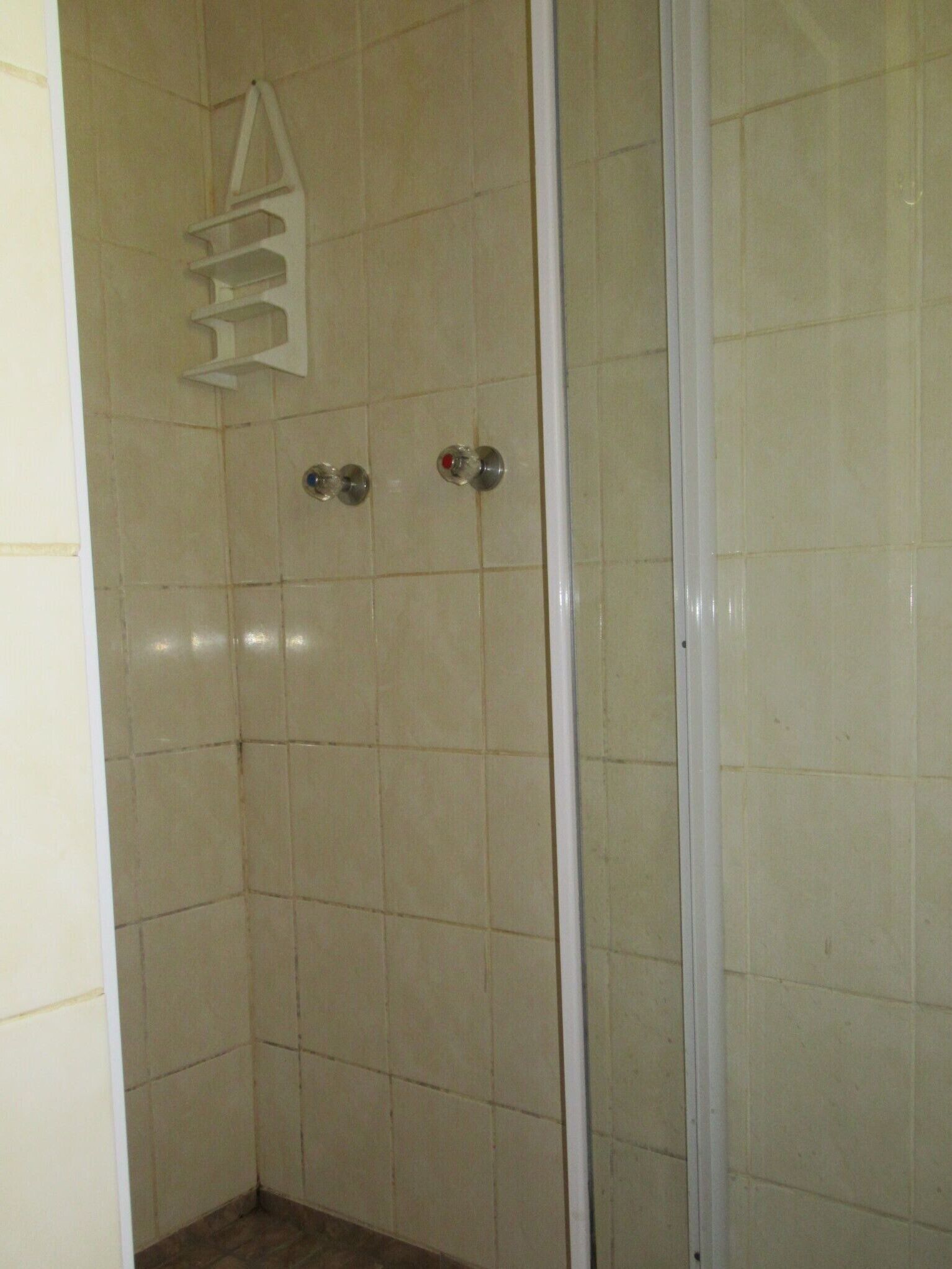 A shower with beige tiles, a white door frame, and a metal shower head.