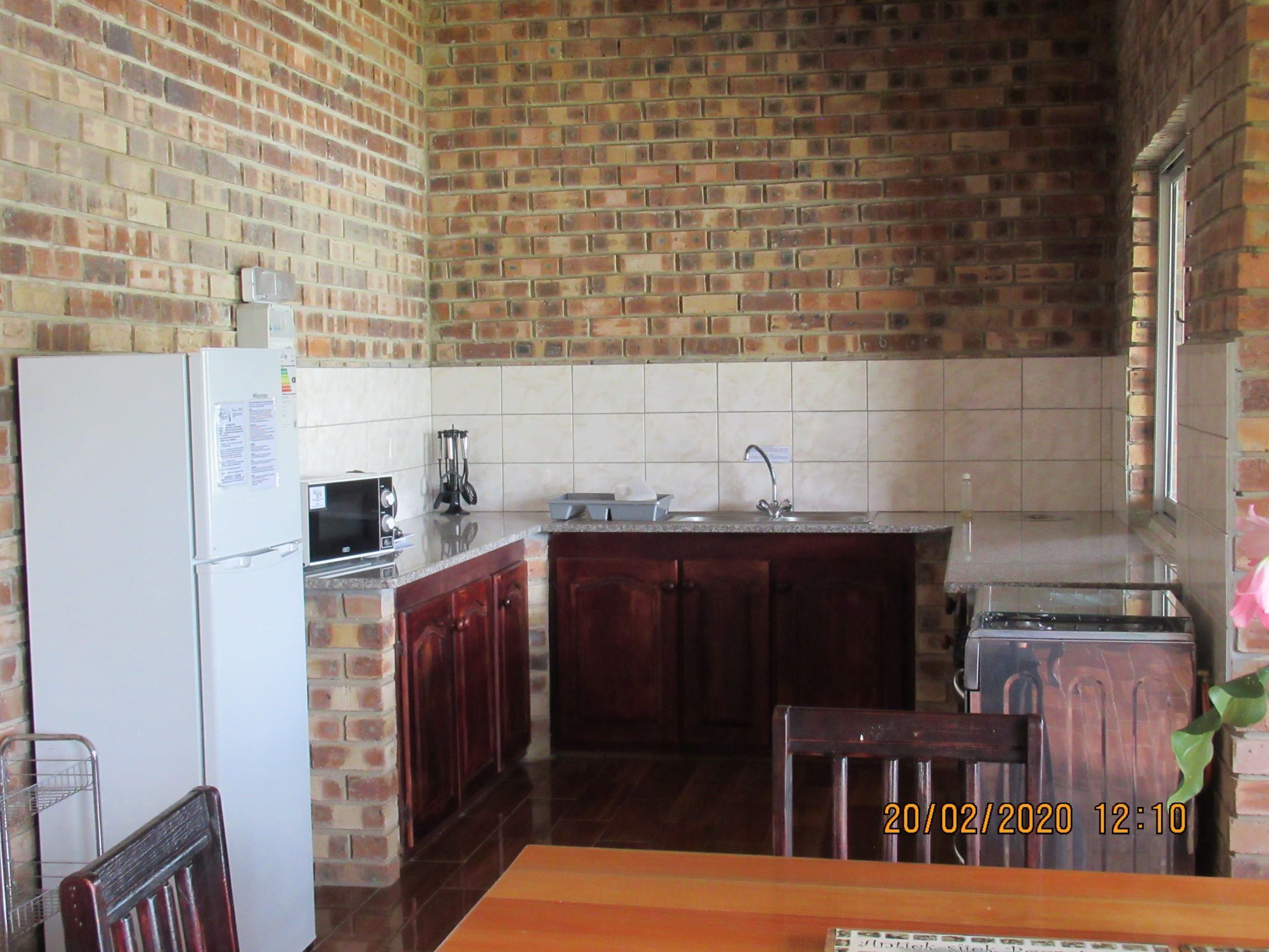 A kitchen with a brick wall, a refrigerator, a microwave, a sink, and wooden cabinets.