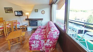 Ein gemütliches Wohnzimmer mit Kamin, einer Couch, Holzmöbeln und einem Balkon mit Sitzgelegenheit.
