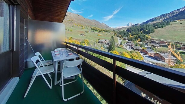 Ein Balkon mit Tisch und Stühlen mit Blick auf ein Tal mit Häusern und Bergen.