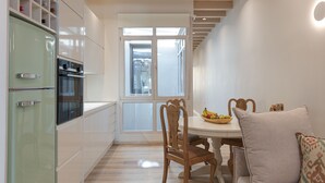 A modern kitchen with white cabinets, a green refrigerator, wooden chairs, and a dining table with a fruit bowl.