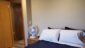 Ein Schlafzimmer mit einem Bett, einem Nachttisch, einem Ventilator und einer Tür zu einem anderen Raum.