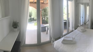 A hotel room with a bed, a chair, a desk, and a balcony with a view of greenery.