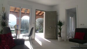 A modern living room with a sofa, a chair, and a table. There are two potted plants and a door leading to another room.