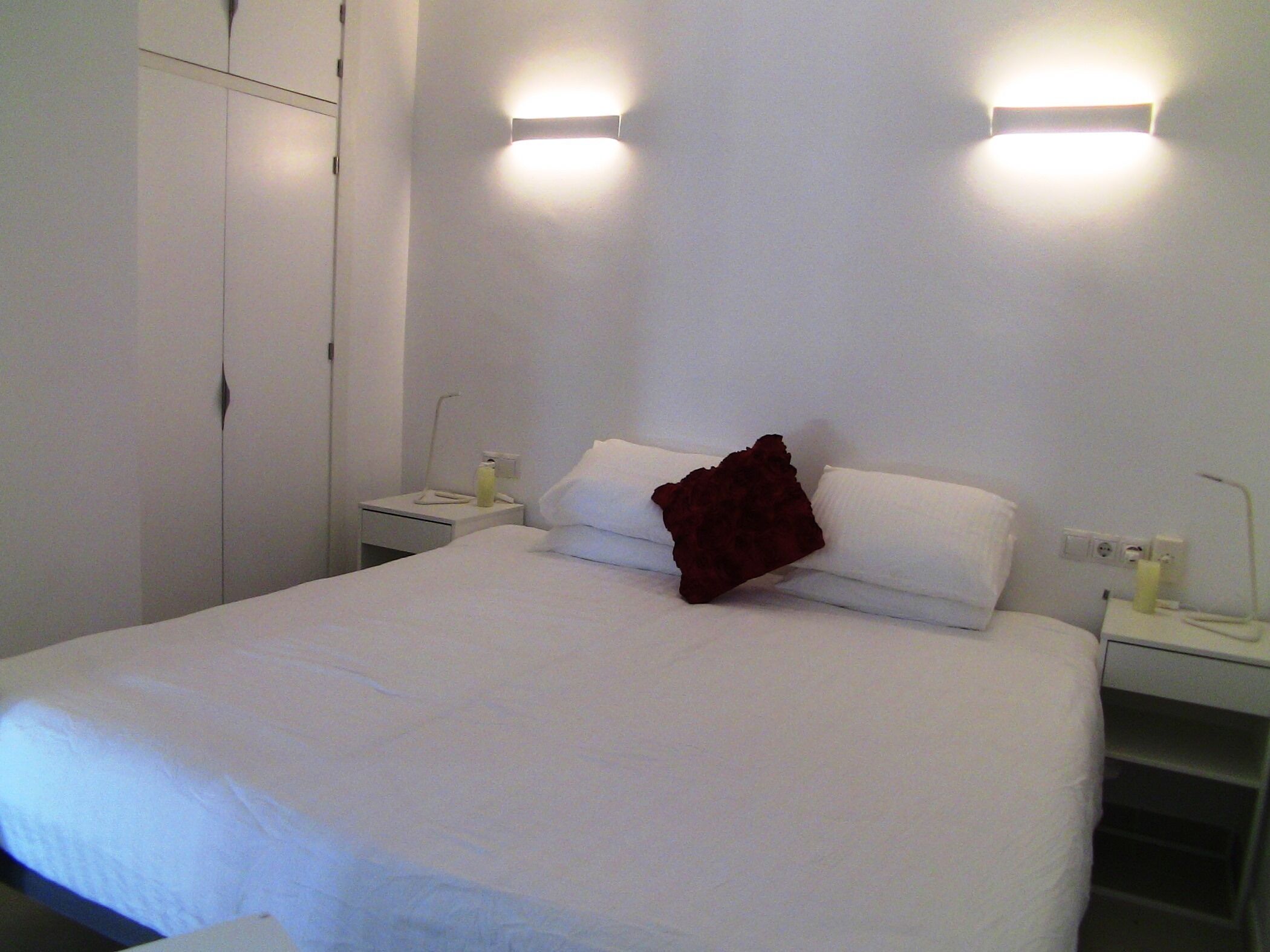 Habitación de hotel con una cama grande, dos mesitas de noche, un armario y lámparas de pared.