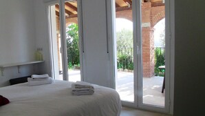 A bedroom with a large bed, a sliding glass door leading to an outdoor area, and a brick structure visible through the door.