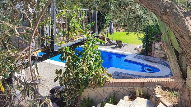 A pool area with a stone deck, lounge chairs, and a view of a garden.