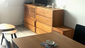 A modern room with a wooden dining table, two chairs, a TV on a wooden cabinet, and decorative wall art. - Bright, functional apartment by the sea (Villers-sur-Mer)