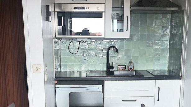 A compact kitchen with white cabinets, a built-in oven, and a stainless steel range hood. - Bright, functional apartment by the sea (Villers-sur-Mer)