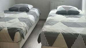 A room with two beds, a sloped ceiling, and a window with curtains. - Bright, functional apartment by the sea (Villers-sur-Mer)