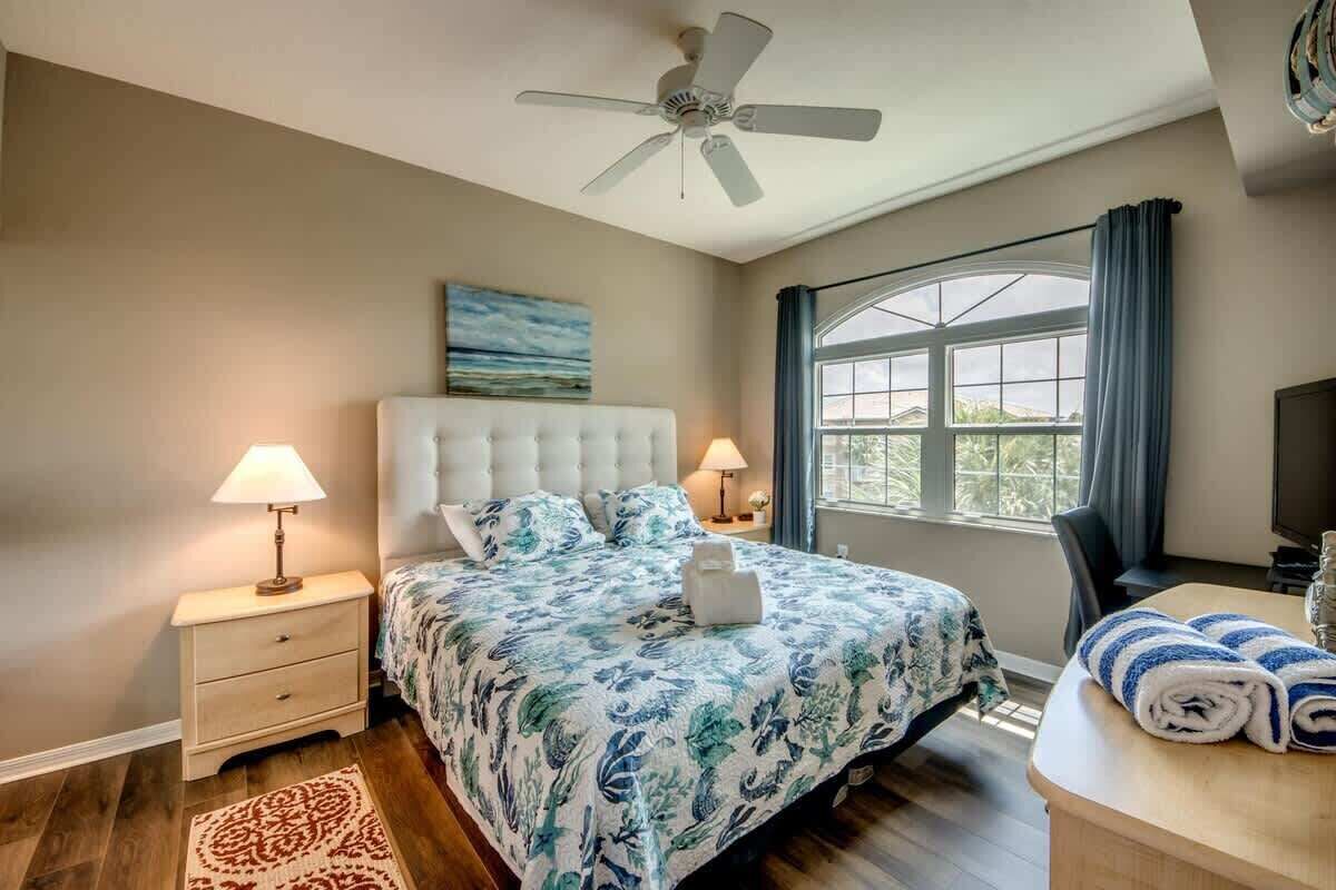 A bedroom with a bed, nightstands, a desk, a ceiling fan, and a window.