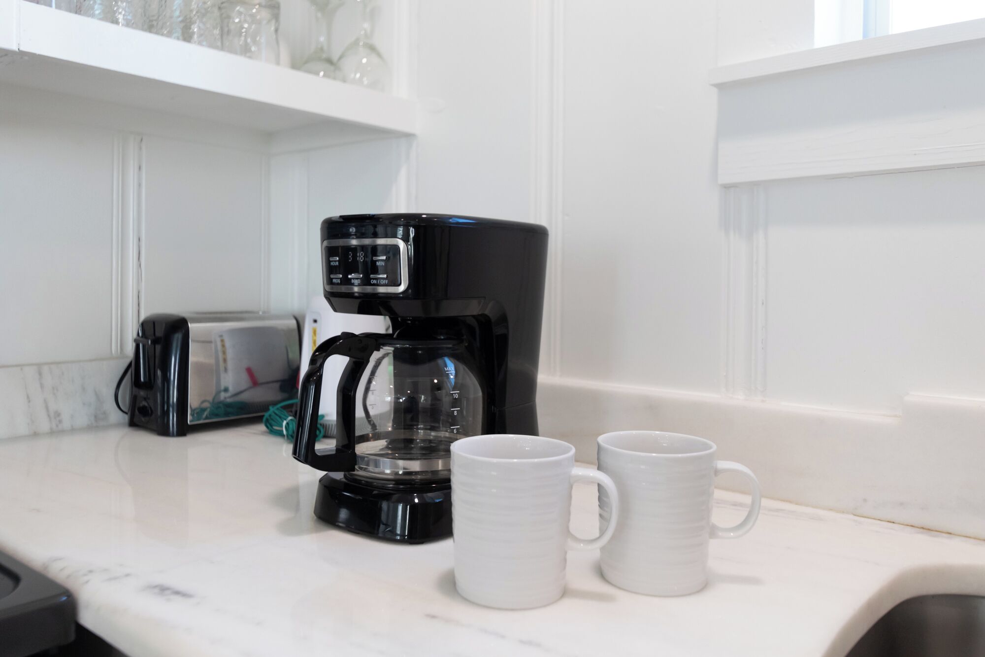 A kitchen counter with a coffee maker, two white mugs, and a toaster.
