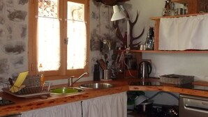 Une cuisine rustique avec des poutres en bois, un mur en pierre, un évier, une cuisinière et une fenêtre donnant sur l’extérieur.
