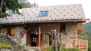 Une maison de campagne en pierre, dotée d’un porche en bois, d’un escalier en pierre et de jardinières suspendues.