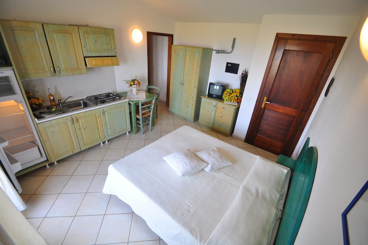 A compact hotel room with a bed, a small kitchenette, a dining area, and a bathroom.