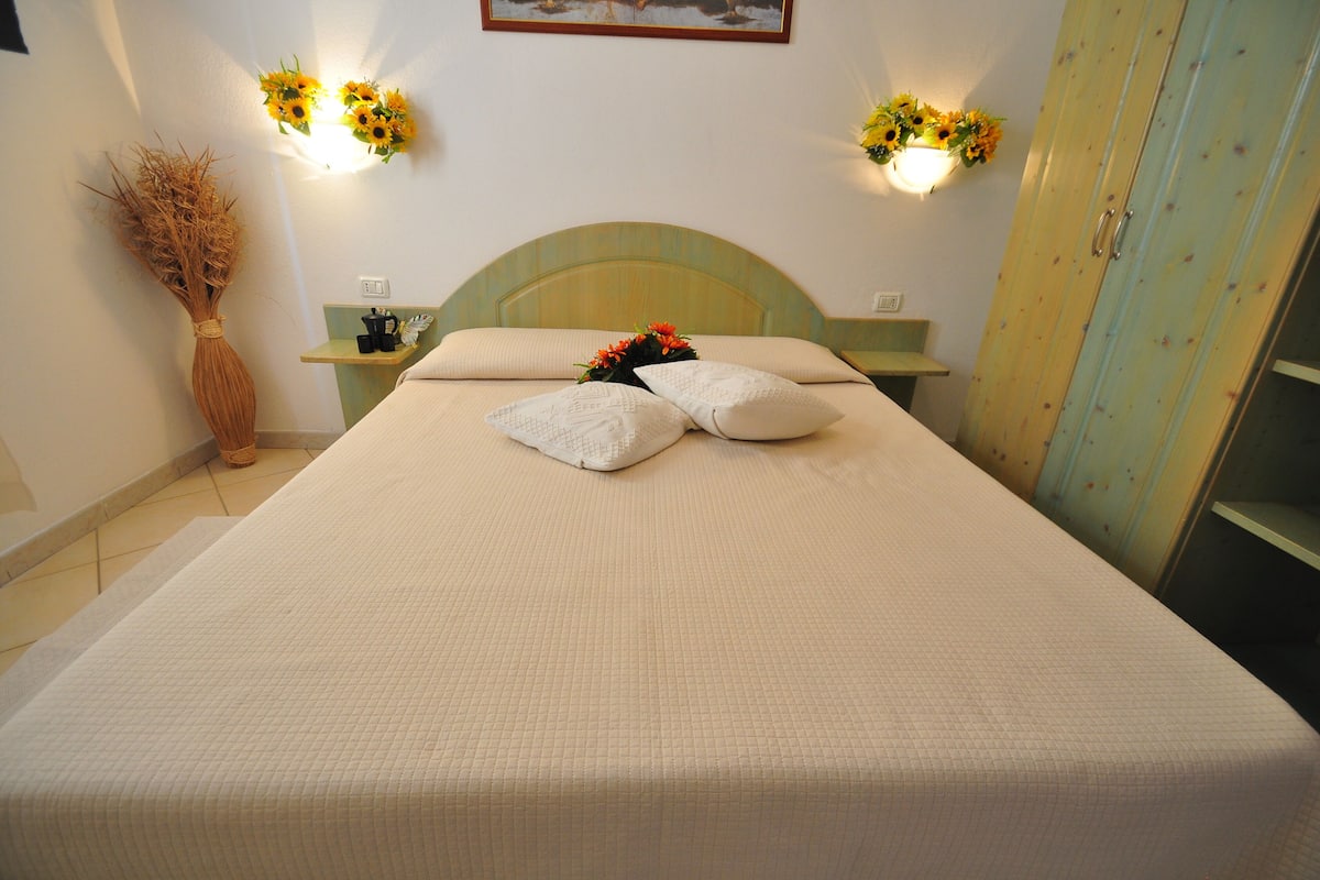 A neatly made bed with a quilted bedspread, two pillows, and a decorative flower arrangement.