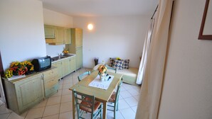A compact kitchen with a dining area, a television on the counter, and a small table with a vase of flowers. - Residenze La Corte (Badesi)