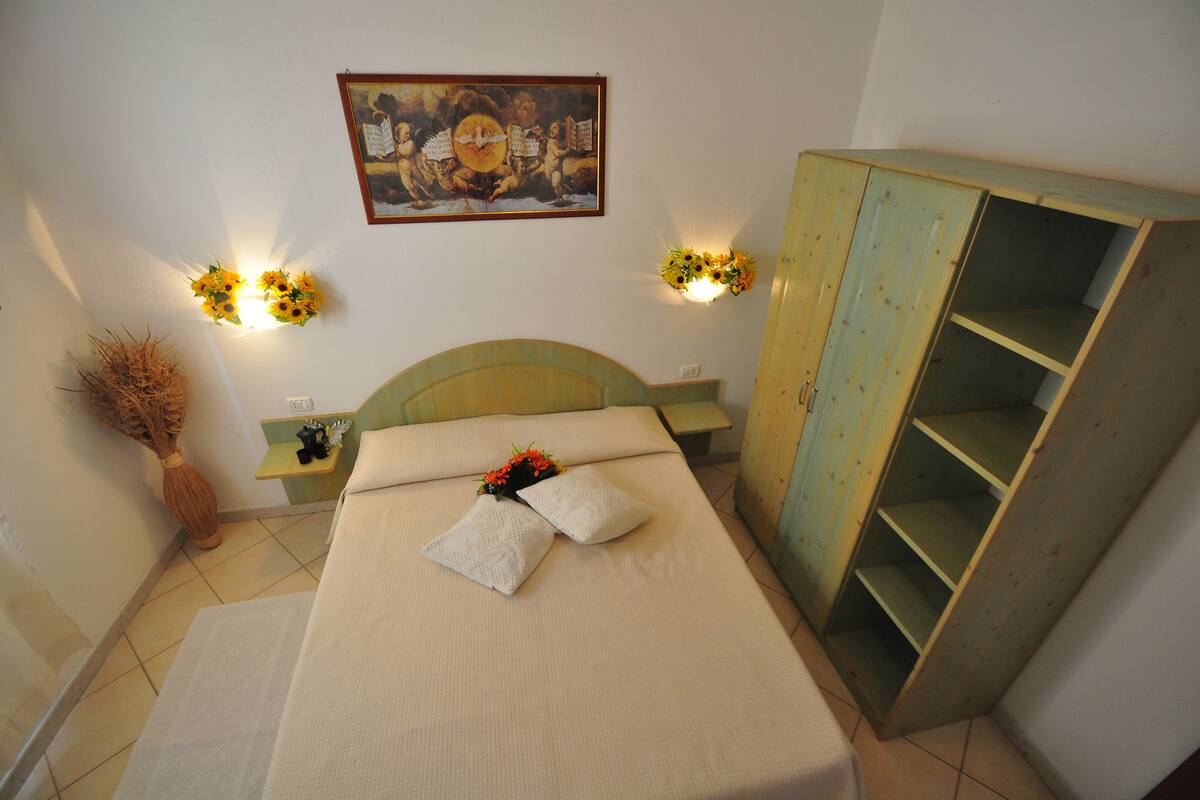 A bedroom with a bed, a nightstand, a wardrobe, and wall-mounted lights.