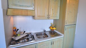 A kitchen with a gas stove, sink, and light green cabinets. - Residenze La Corte (Badesi)