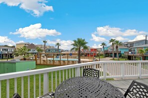 A deck with a pool, palm trees, and a view of a residential area.