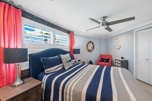 Un dormitorio con una cama, una mesita de noche, una silla, un ventilador de techo y una puerta.