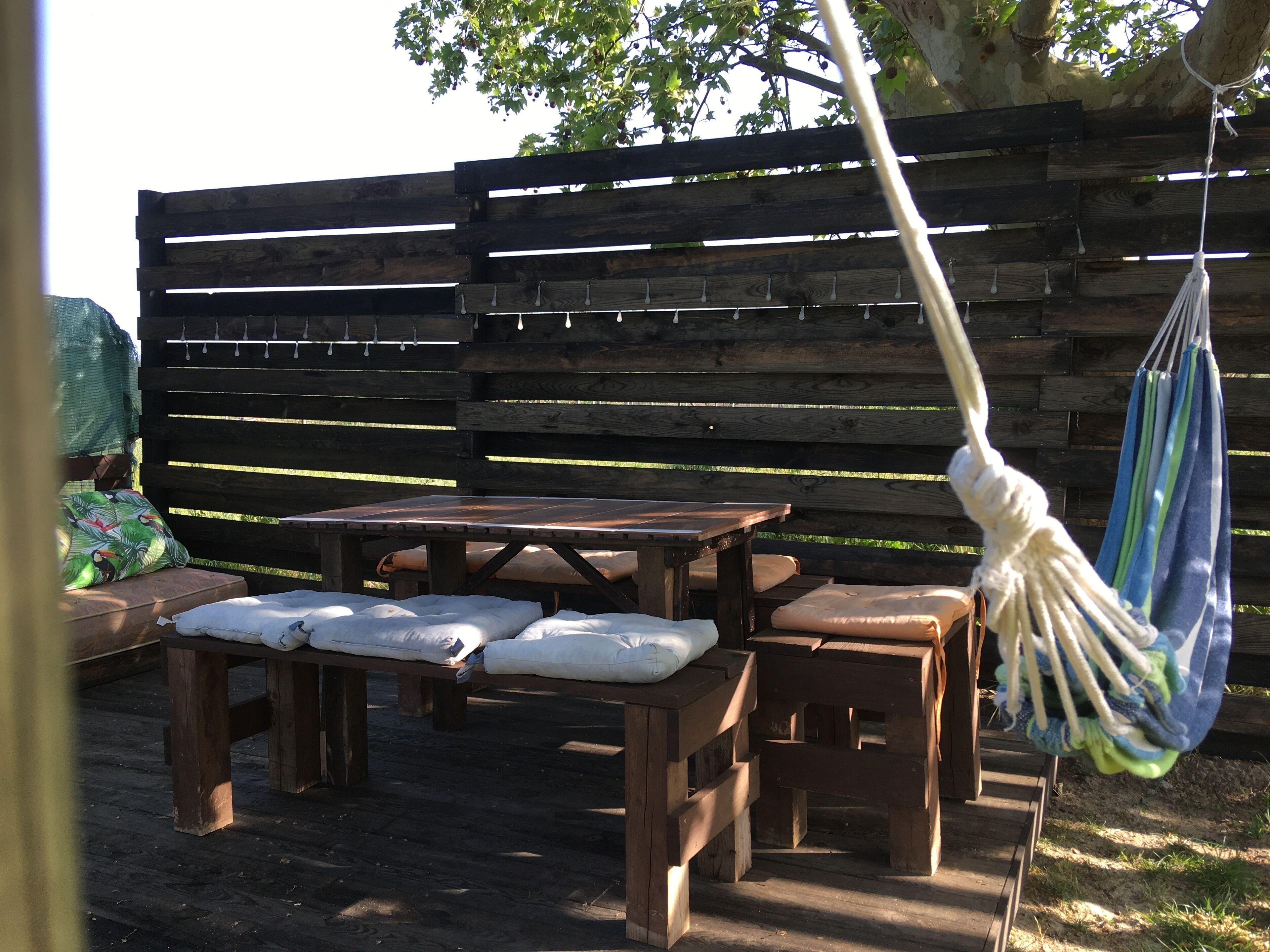 A wooden outdoor seating area with benches and a table, surrounded by a wooden fence.