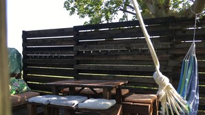 Un espace extérieur aménagé en bois, avec des bancs et une table, entouré d’une clôture en bois.
