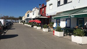 Une rue bordée de voitures garées et de terrasses de cafés.