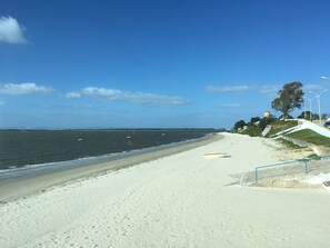 Een strand met een heldere lucht, een zandstrand en enkele boten op het water.