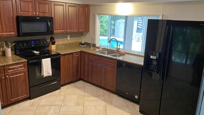 A modern kitchen with wooden cabinets, a black refrigerator, a microwave, and a stove. - 3 bedroom, 2 bathroom private pool home just minutes from Siesta Key! (Sarasota)