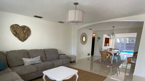 A spacious living area with a grey sofa, a white coffee table, and a dining area with a pool view. - 3 bedroom, 2 bathroom private pool home just minutes from Siesta Key! (Sarasota)