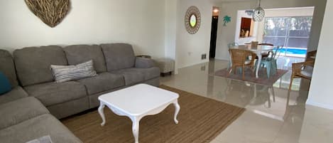 Un salón amplio con un sofá gris, una mesa de centro blanca y un comedor con vista a la piscina.