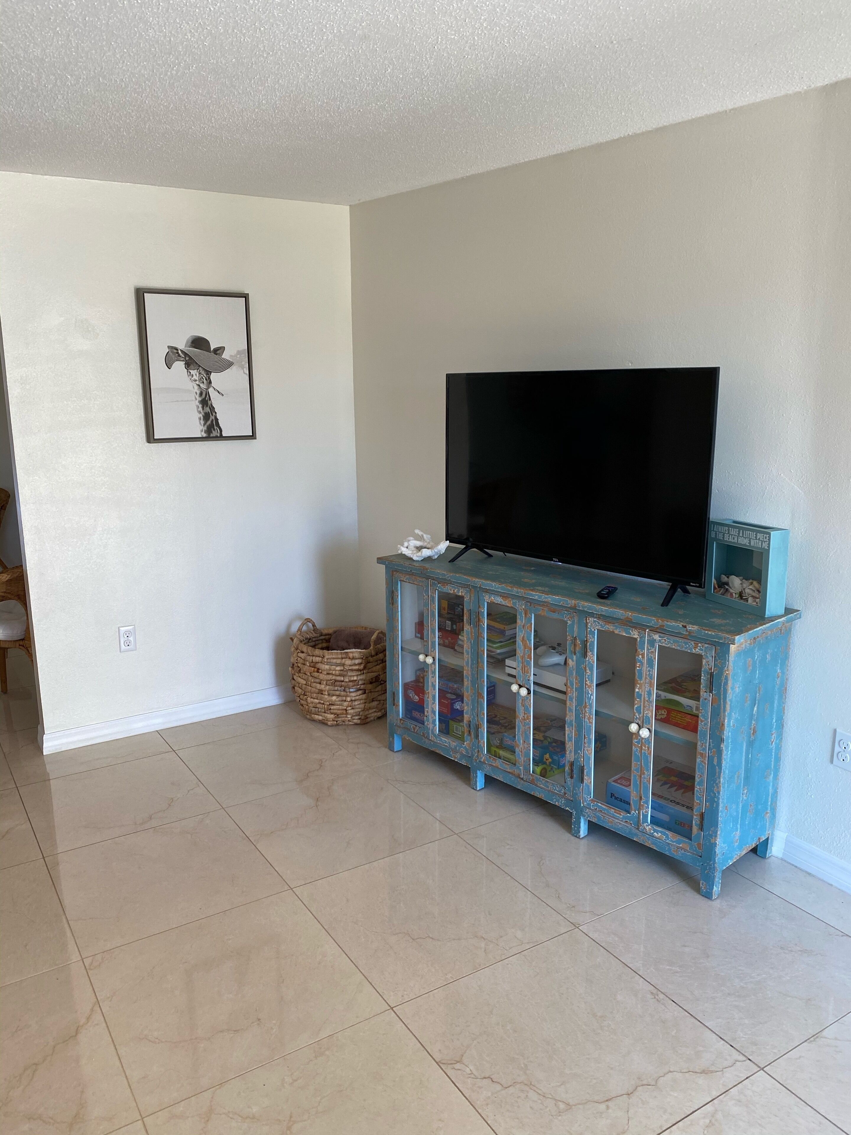Una sala de estar con un televisor sobre un mueble azul, un cuadro en la pared y una cesta de mimbre en el suelo.
