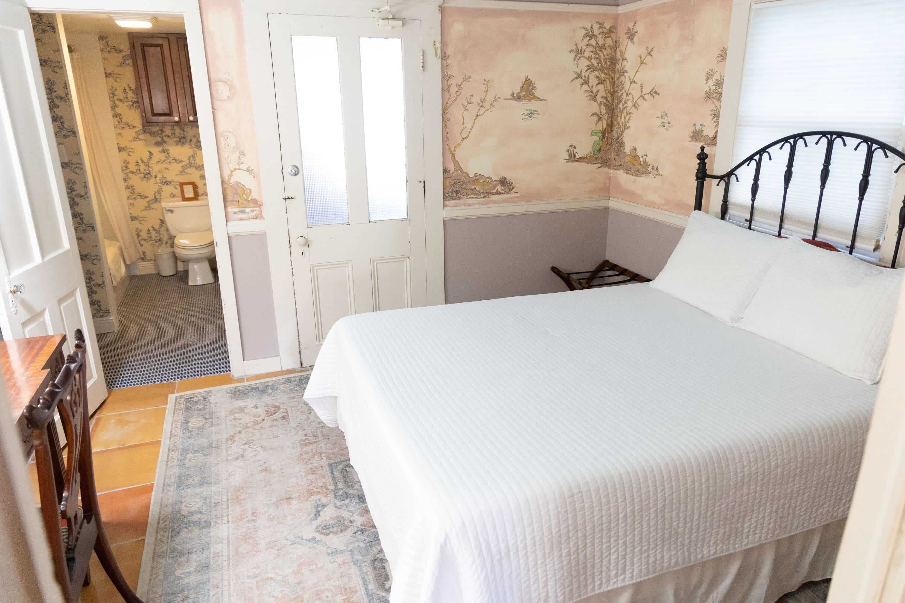 Une chambre à coucher avec un lit, une chaise en bois, un tapis, une salle de bain avec des toilettes et une porte.