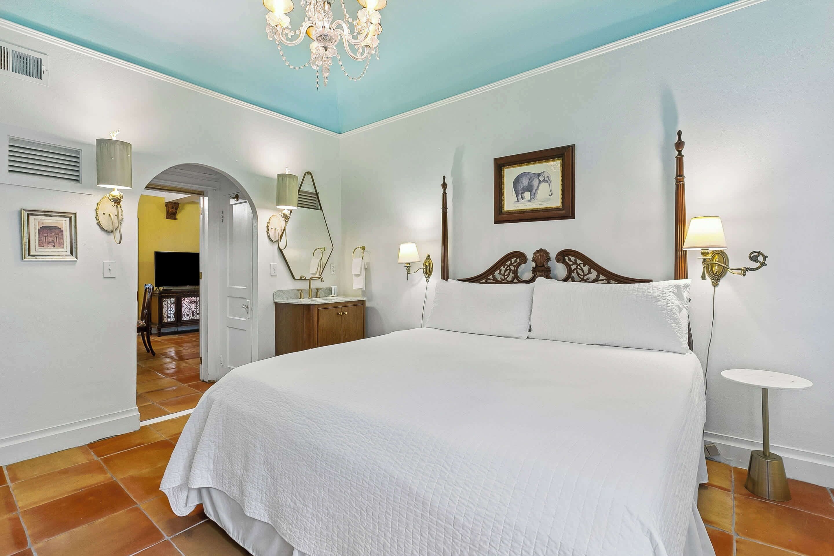 Une chambre à coucher avec un grand lit, un lustre, une table de chevet et un tableau au mur.