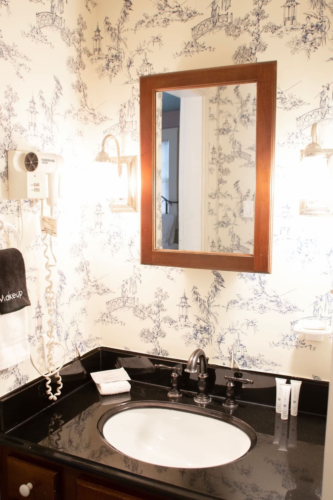 Une salle de bain avec un lavabo noir, un miroir avec un cadre en bois et un mur orné d’un motif floral.
