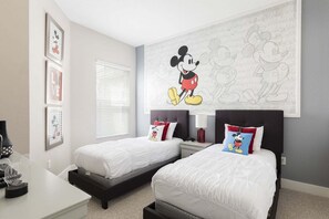 Et soveværelse med to senge, et stort vægmaleri med Mickey Mouse, et skrivebord med en computer og et vindue med skodder.