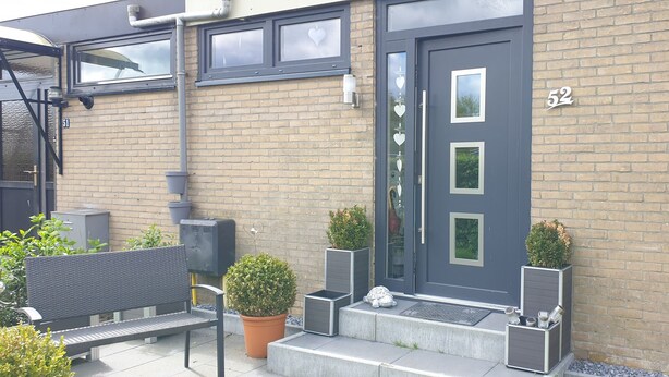 A modern building with a dark gray door, numbered 52, and a brick facade.
