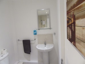Un baño con un lavamanos blanco, un espejo encima y un perchero para toallas.