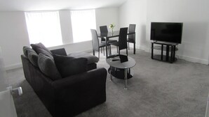 Una sala moderna con un sofá negro, una mesa de centro, una mesa de comedor con sillas y un televisor de pantalla plana.