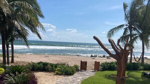 Ein steiniger Weg führt zu einem Strand mit Palmen und Blick auf den Ozean.