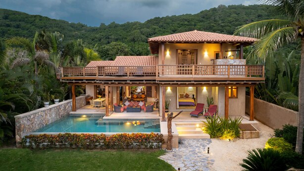 Ein zweistöckiges Haus mit Pool, Sitzgelegenheiten im Freien und Blick auf den Wald.