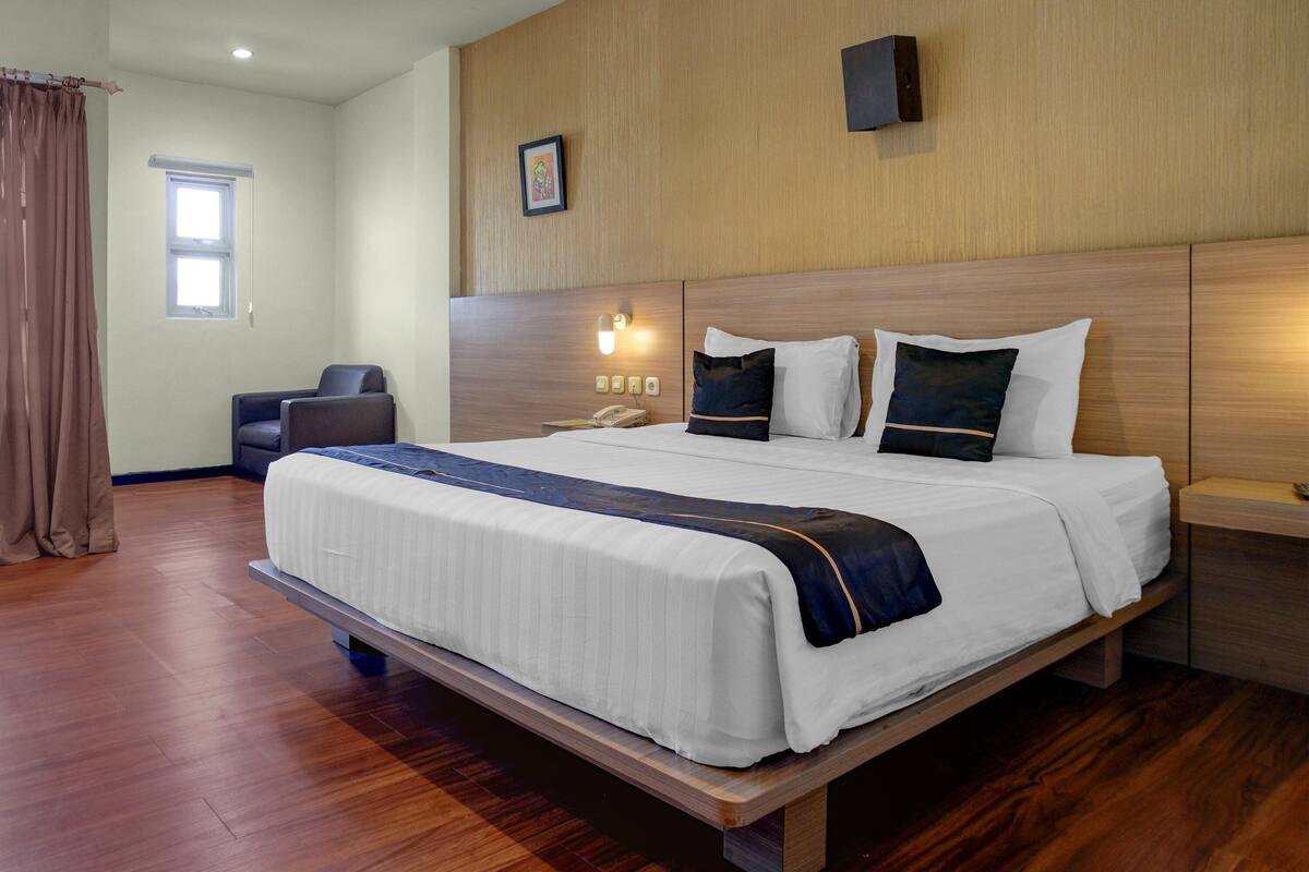 Une chambre d’hôtel avec un grand lit, un bureau, une chaise, une table de chevet et une fenêtre avec des rideaux.