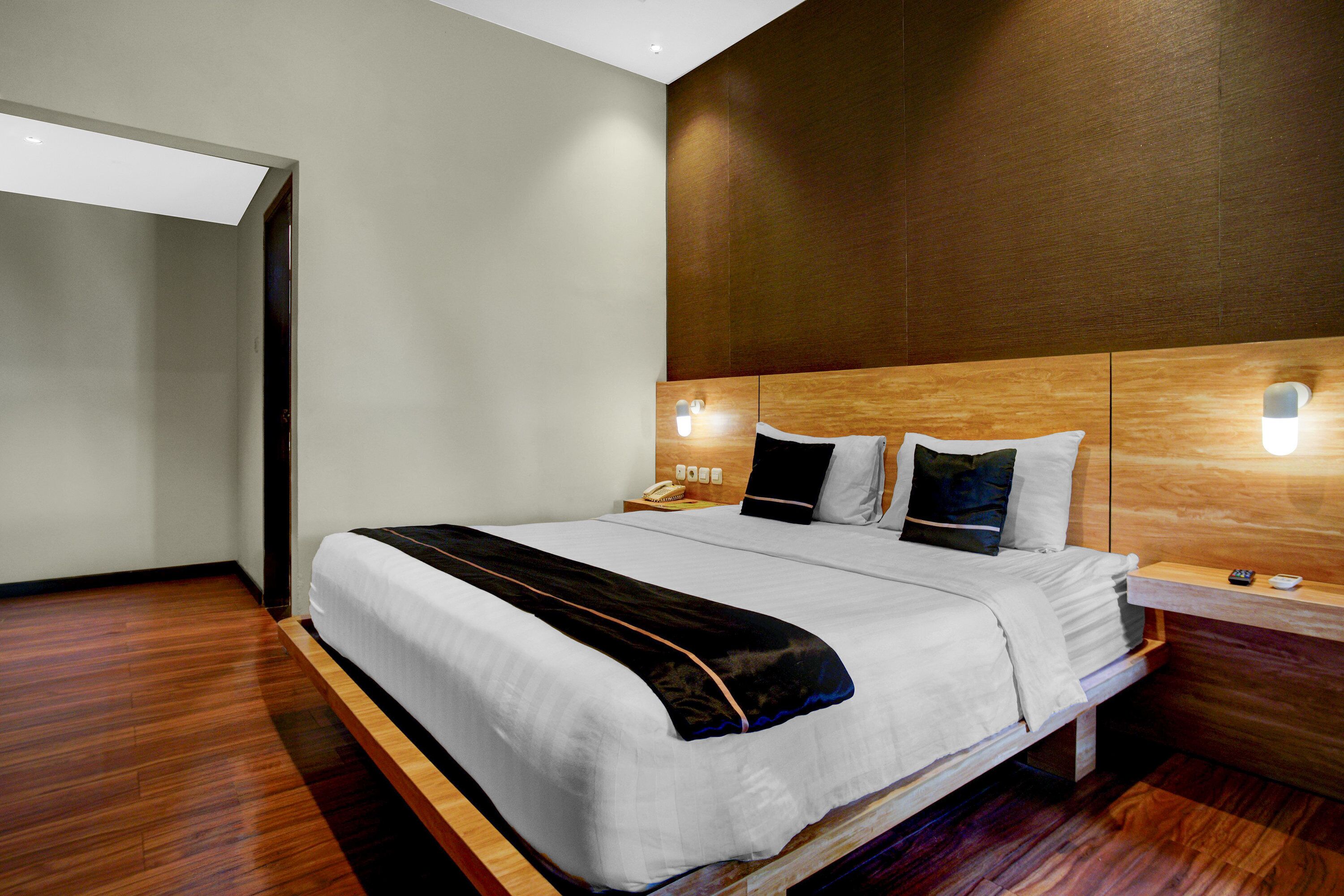 A modern hotel room with a large bed, wooden headboard, bedside lamps, and a wooden floor.