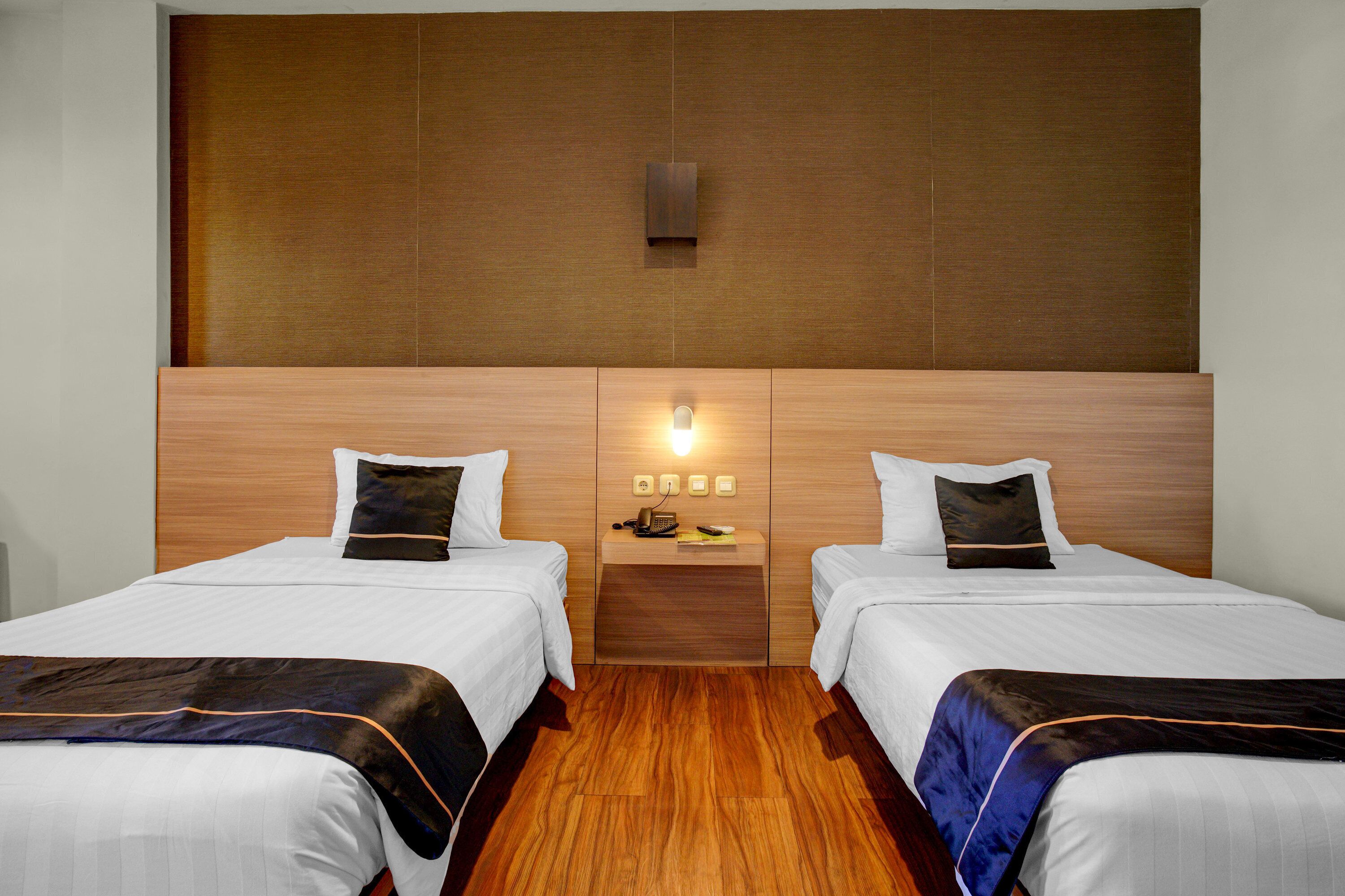 A hotel room with two beds, wooden headboard, bedside tables with lamps, and a wooden floor.
