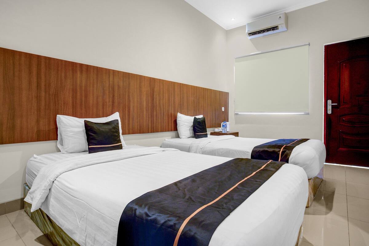 Une chambre d’hôtel avec deux lits, une tête de lit en bois, un tableau blanc et une porte rouge.