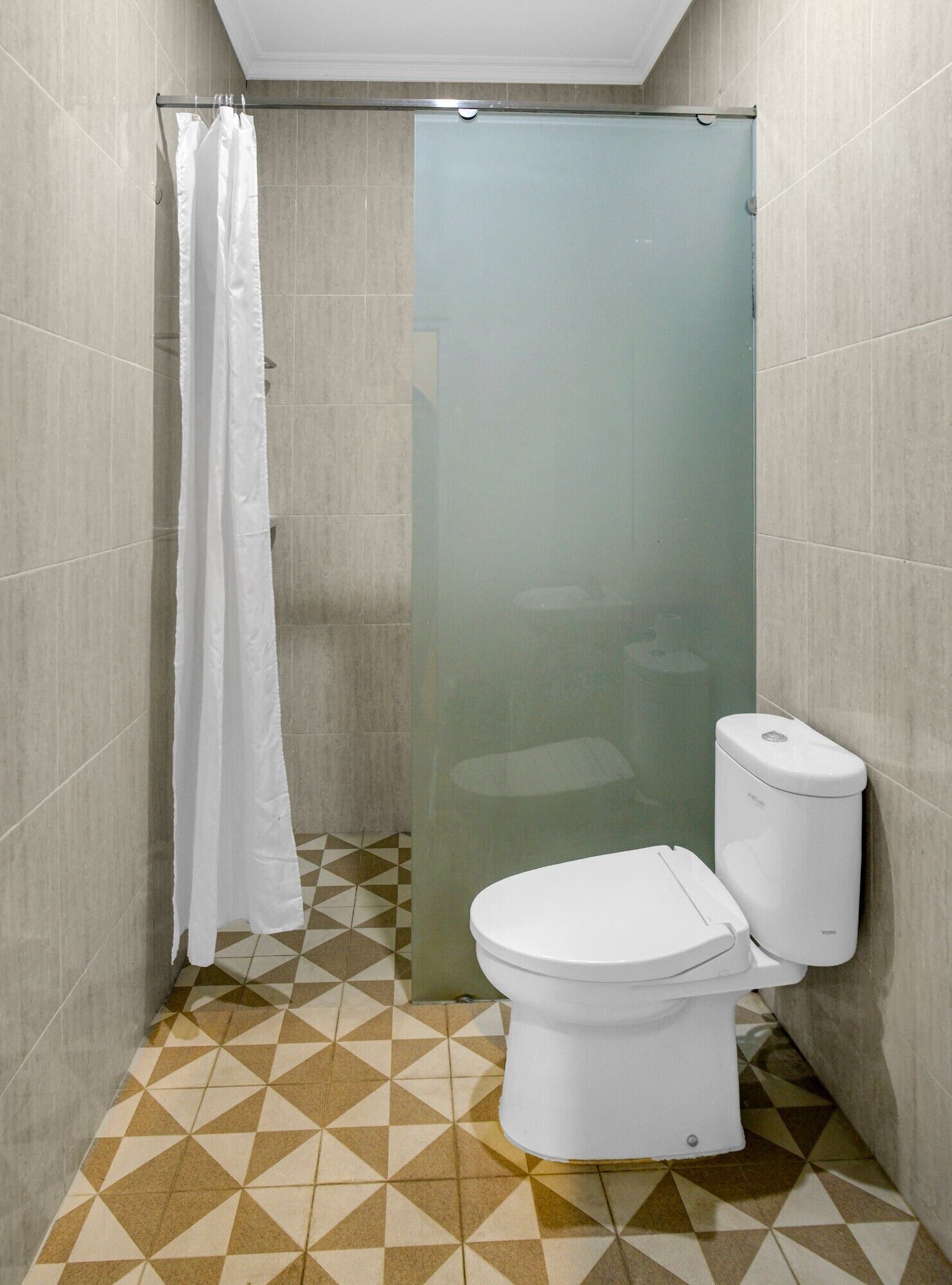 A small bathroom with a toilet, a shower with a glass door, and a patterned floor.