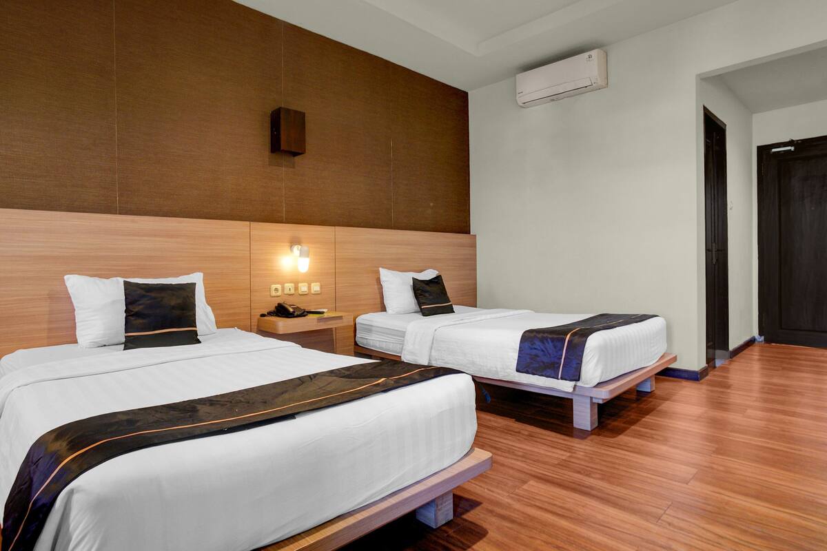 Une chambre d’hôtel avec deux lits, une tête de lit en bois, une table de chevet, un téléphone et un appareil de climatisation.