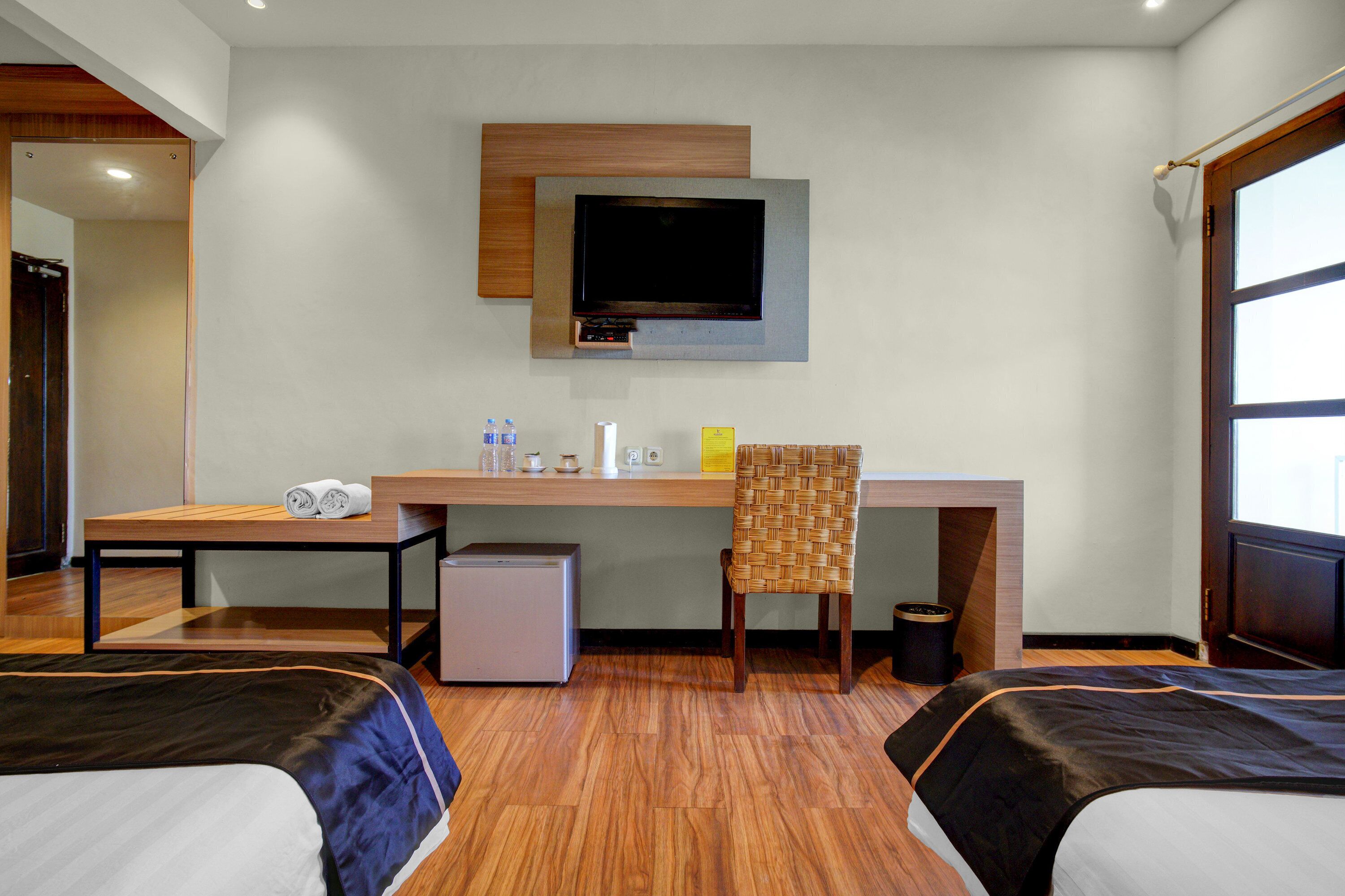 A hotel room with two beds, a desk, a chair, a TV, and a small trash bin.