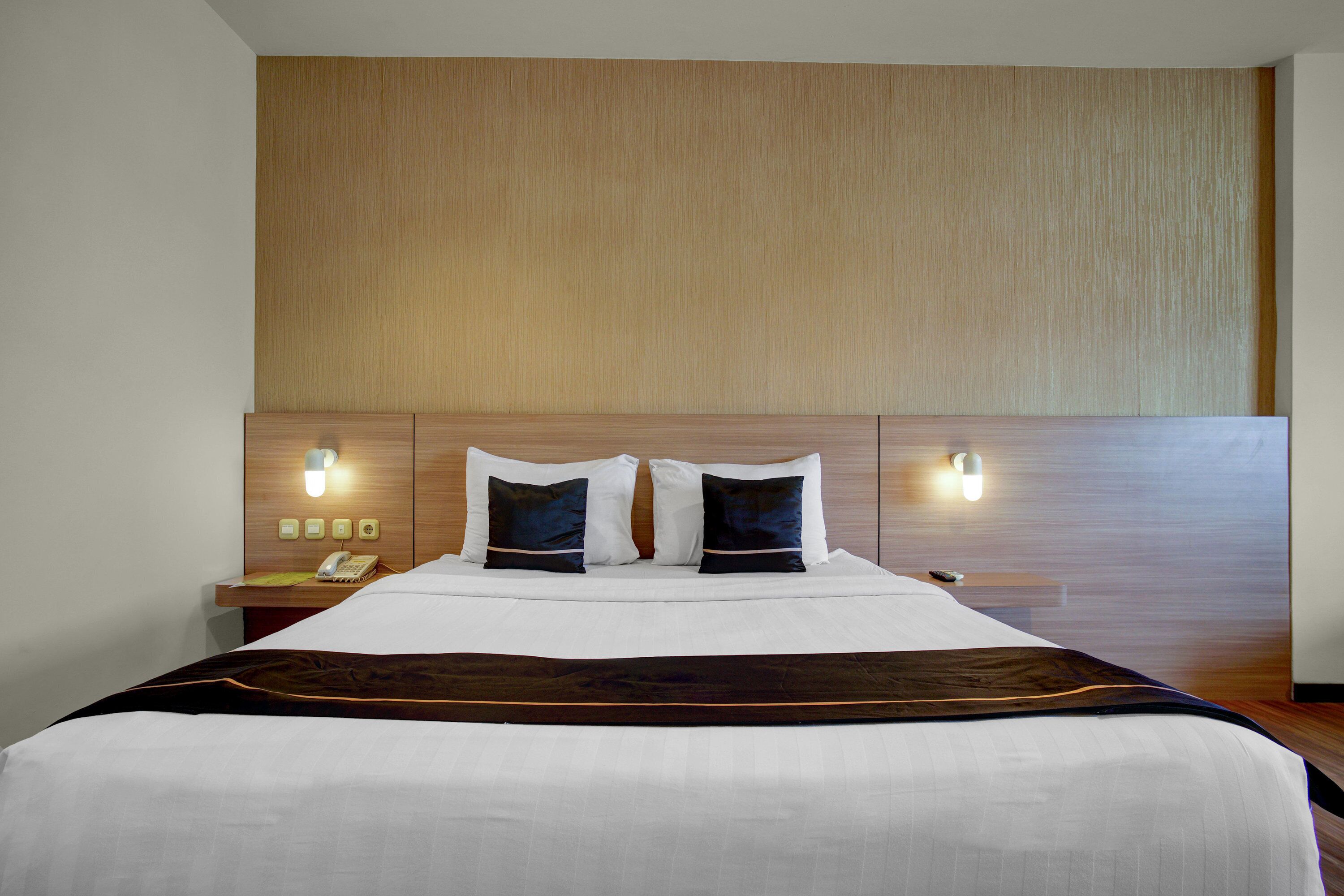 A hotel room with a large bed, two bedside tables, a wooden headboard, and wall-mounted lights.